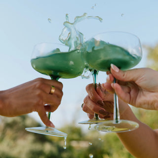 Two people clinking Mojito brain powder together outdoors with a blurred natural background