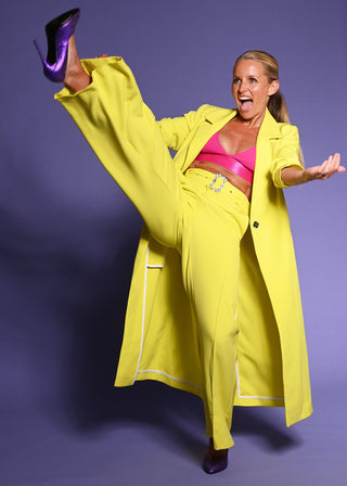 Davinia Taylor kicking a yellow suit on a purple background  