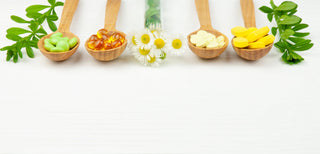 4 wooden spoons filled with colorful tablets, capsules, and vitamins. With green leaves and flowers