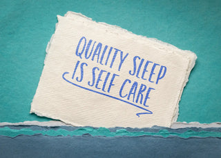 A textured piece of paper on a blue background reading "QUALITY SLEEP IS SELF CARE". The edges of the paper and background fabric are torn and layered.