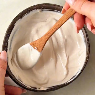 Person holding a wooden spoon in a bowl of white creamy substance
