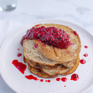 Stack of pancakes with red berry sauce on a white plate