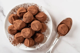 Plate with multiple chocolate protein balls, spoon with single chocolate protein ball to the right