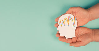 Two hands hold a paper cutout of a human head with colorful, wavy lines inside it, representing epilepsy