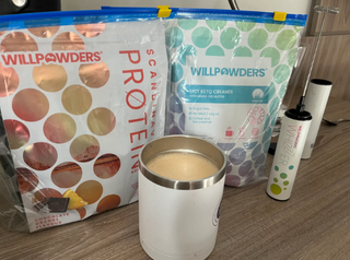 2 bags of WillPowders Chocolate orange protein, MCR Keto Creamer and Whizzer. With a coffee in the foreground