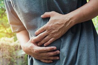 A person wearing a grey shirt is holding their stomach with both hands, suggesting they might be experiencing abdominal pain