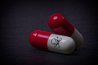 Two red and white capsules, one with a skull and crossbones symbol, lie on a dark surface. The symbol indicates a warning, potentially suggesting that the capsules are harmful or toxic.