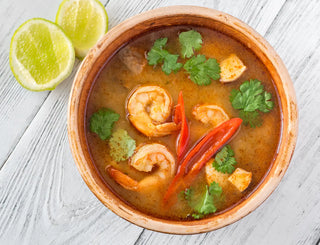 A orange bowl of Prawn Pho with lime on a white wooden table