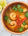 A orange bowl of Prawn Pho with lime on a white wooden table