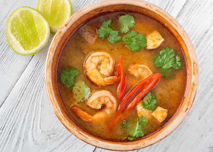 A orange bowl of Prawn Pho with lime on a white wooden table