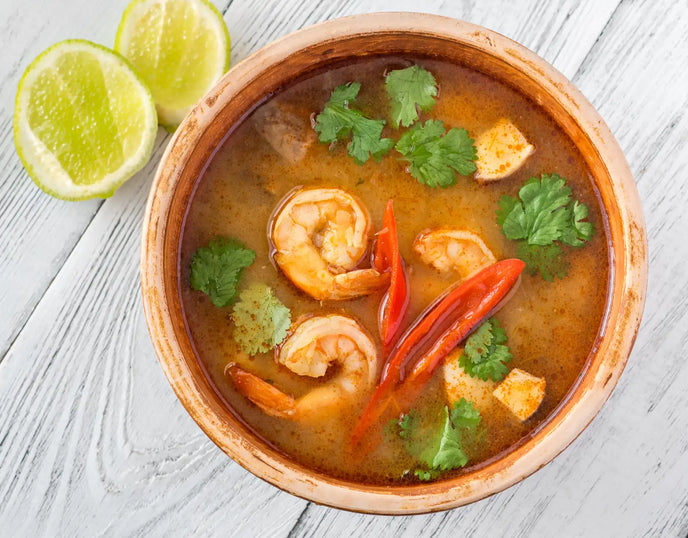 A orange bowl of Prawn Pho with lime on a white wooden table