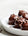 Chocolate covered protein balls topped with nuts on a white plate and on a white background 