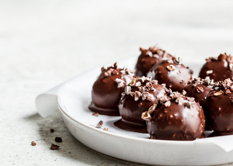Chocolate covered protein balls topped with nuts on a white plate and on a white background 