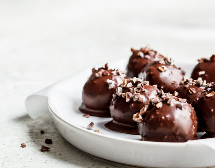 Chocolate covered protein balls topped with nuts on a white plate and on a white background 