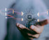 A person's hand is extended forward, with a floating microchip labeled "AI" in the center. The microchip is connected to lines symbolizing data flow, merging and splitting with other chips. The background is blurred, drawing focus to the AI element in the hand.