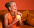 Willpowders founder Davinia Taylor laughing with a yellow drink, sitting on an orange sofa on an orange background 