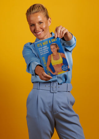 Davinia Taylor wearing blue, holding her book 'It's Not a Diet' on an orange background 