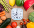 A clock surrounded by various vegetables and fruits on a brown background