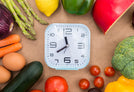 A clock surrounded by various vegetables and fruits on a brown background