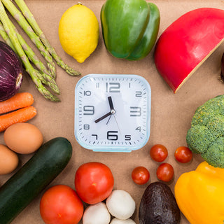 A clock surrounded by various vegetables and fruits on a brown background