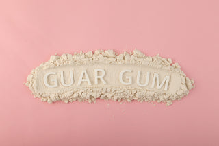 Loose guar gum powder on a light pink surface. The words "GUAR GUM" are in the center