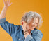 A woman with curly gray hair smiling standing in front of an orange background.