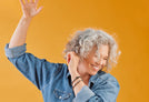 A woman with curly gray hair smiling standing in front of an orange background.