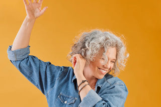 A woman with curly gray hair smiling standing in front of an orange background.
