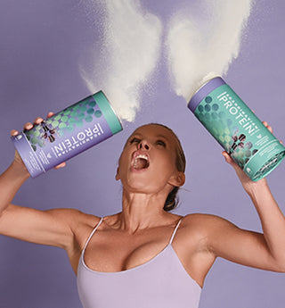 WillPowders founder Davinia Taylor shaking two tubs of protein powder, creating a cloud above her head against a purple background