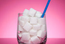 A glass with a blue plastic straw in filled with sugar cubes