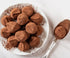 Plate with multiple chocolate protein balls, spoon with single chocolate protein ball to the right