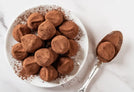 Plate with multiple chocolate protein balls, spoon with single chocolate protein ball to the right