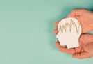 Two hands hold a paper cutout of a human head with colorful, wavy lines inside it, representing epilepsy