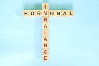 Wooden letter tiles spell "HORMONAL" horizontally and "IMBALANCE" vertically on a light blue background.