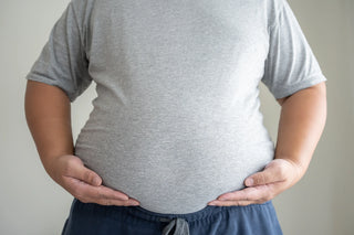 A person wearing a gray t-shirt and navy blue pants holding their stomach with both hands
