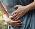 A person wearing a grey shirt is holding their stomach with both hands, suggesting they might be experiencing abdominal pain