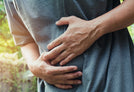 A person wearing a grey shirt is holding their stomach with both hands, suggesting they might be experiencing abdominal pain