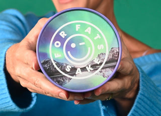 Woman holding a Protein Powder tub showing the lid with the text For Fats Sake, white text on a mountain range background