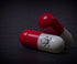 Two red and white capsules, one with a skull and crossbones symbol, lie on a dark surface. The symbol indicates a warning, potentially suggesting that the capsules are harmful or toxic.